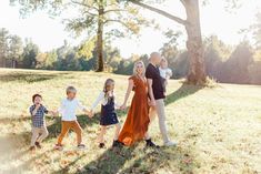 a family holding hands and walking through the grass in front of a tree at sunset