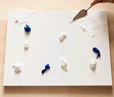 someone is using a knife to cut out small pieces of white and blue paint on a piece of paper