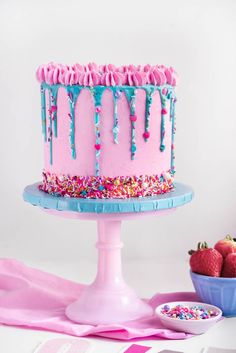 a pink cake with sprinkles and blue icing sitting on top of a table