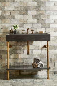 a bathroom sink sitting under a mirror next to a wall mounted faucet in front of a brick wall