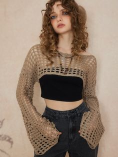 a woman with curly hair wearing a cropped top and jeans, standing in front of a wall