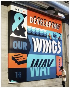 a man is standing in front of a large sign that says, we are developing our wings and the way