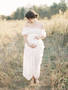 a pregnant woman in a white dress walking through tall grass