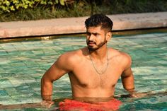 a man standing in the middle of a pool with no shirt on, wearing a chain around his neck