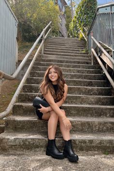 a woman sitting on the steps in front of some stairs with her legs crossed and wearing black boots