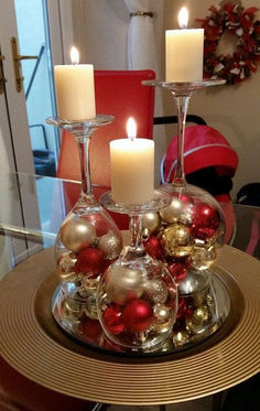 two wine glasses filled with ornaments on top of a glass table topped with candles and christmas balls