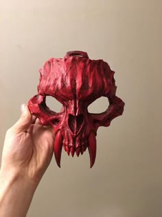 a hand holding up a red mask that looks like a demon's skull