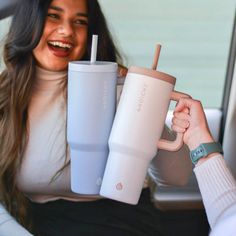 a woman holding two tumblers in her hand while sitting in the back seat of a car