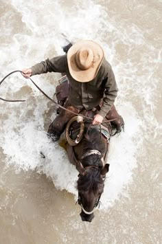 a man riding on the back of a brown horse in water with a lasso