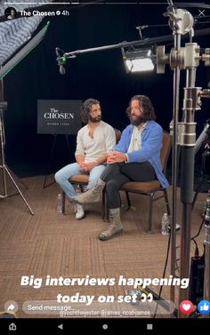 two men sitting in chairs talking to each other with microphones and lights behind them