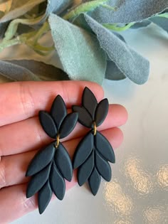 a pair of black earrings sitting on top of a person's hand next to green leaves