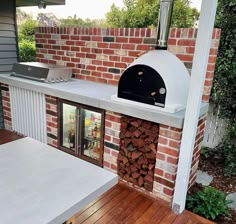 an outdoor pizza oven built into the side of a brick building with wood stacked on top