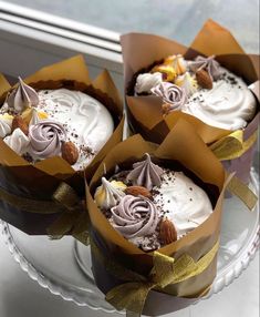 three cakes with white frosting and brown ribbons on a glass platter next to a window