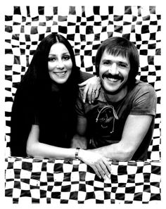 a man and woman posing for a photo in front of a checkered wall with black and white squares