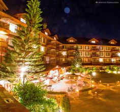 an outdoor area at night with lit up buildings and trees in the foreground, surrounded by lights