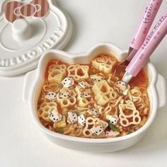 a bowl filled with noodles and dices on top of a white table next to two pink chopsticks