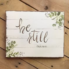 a wooden sign that says be still with flowers and leaves painted on the front side