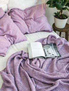 an open book sitting on top of a bed next to pillows and a plant in a pot