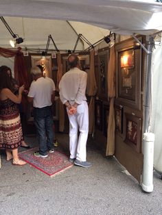 two men and a woman standing under a tent with pictures on the wall behind them