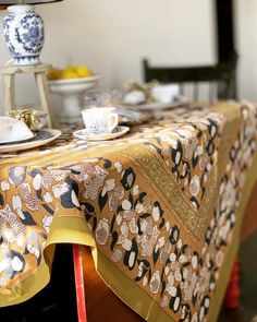 the table is covered with an elaborately designed cloth and has two cups on it