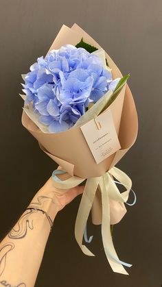 a person's hand holding a bouquet of blue flowers with a tag on it