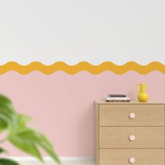 a pink and yellow room with a dresser, potted plant and wall decal