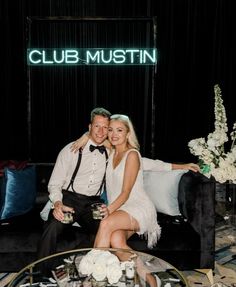 a man and woman sitting on a couch in front of a sign that says club mustin