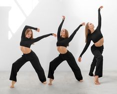 three women in black outfits are doing yoga poses with their arms up and legs spread out