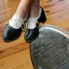 a woman's feet in black and white shoes on top of a metal object