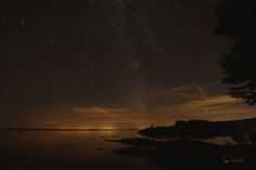 the night sky is lit up with stars and clouds over a calm body of water