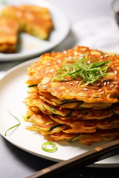 a stack of pancakes on a white plate with green garnish and chopsticks