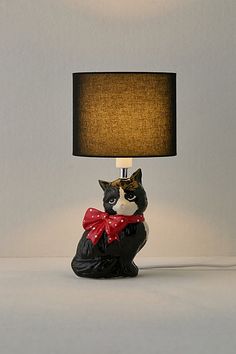 a black and white cat lamp with a red bow on it's chest sitting under a shade