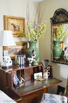 two green vases with flowers on top of a wooden desk next to a mirror