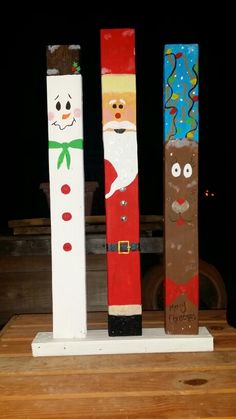 three wooden poles decorated with santa, snowman, and reindeer faces on top of a table