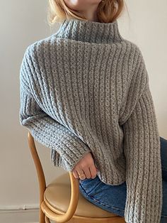 a woman sitting on top of a wooden chair wearing a gray sweater and blue jeans