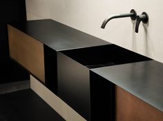 a sink with two faucets on the side and a black counter top underneath it