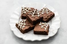 four pieces of brownie on a white plate with spider web decorations and icing