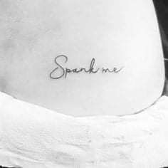 a woman's stomach with the word spank me tattooed on her lower back