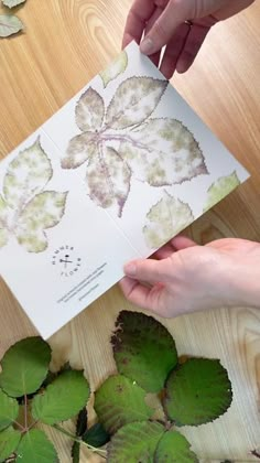 two hands are holding up a card with leaves on it and another hand is reaching for the paper