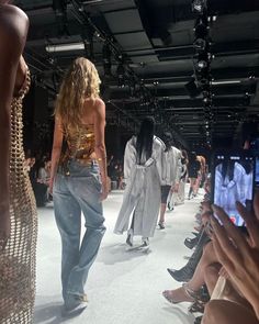 several models walking down the runway with their cell phones in front of them and onlookers