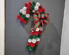 a christmas wreath made out of pine cones and red and white flowers on a gray wall