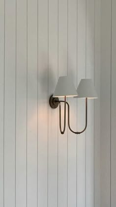 a wall light with two lamps on it in a room that has white paneled walls