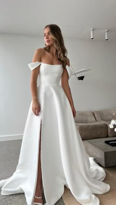 a woman wearing a white dress standing in front of a couch and looking at the camera