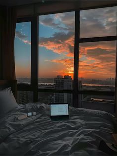 a laptop computer sitting on top of a bed in front of a window at sunset