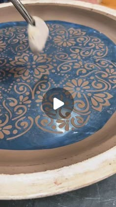 a person is using a brush to paint a blue and gold design on a bowl