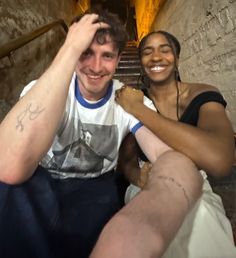 a man and woman sitting on the stairs in an old building smiling at the camera