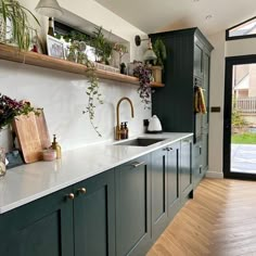 a kitchen with green cabinets and white counter tops, plants on the shelf above the sink