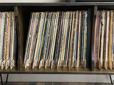 a book shelf filled with lots of different colored records on top of wooden shelves next to a wall