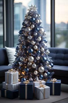 a christmas tree with presents under it in front of a couch and large window overlooking the city