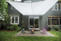 a patio with chairs and an awning in front of a gray house on a sunny day